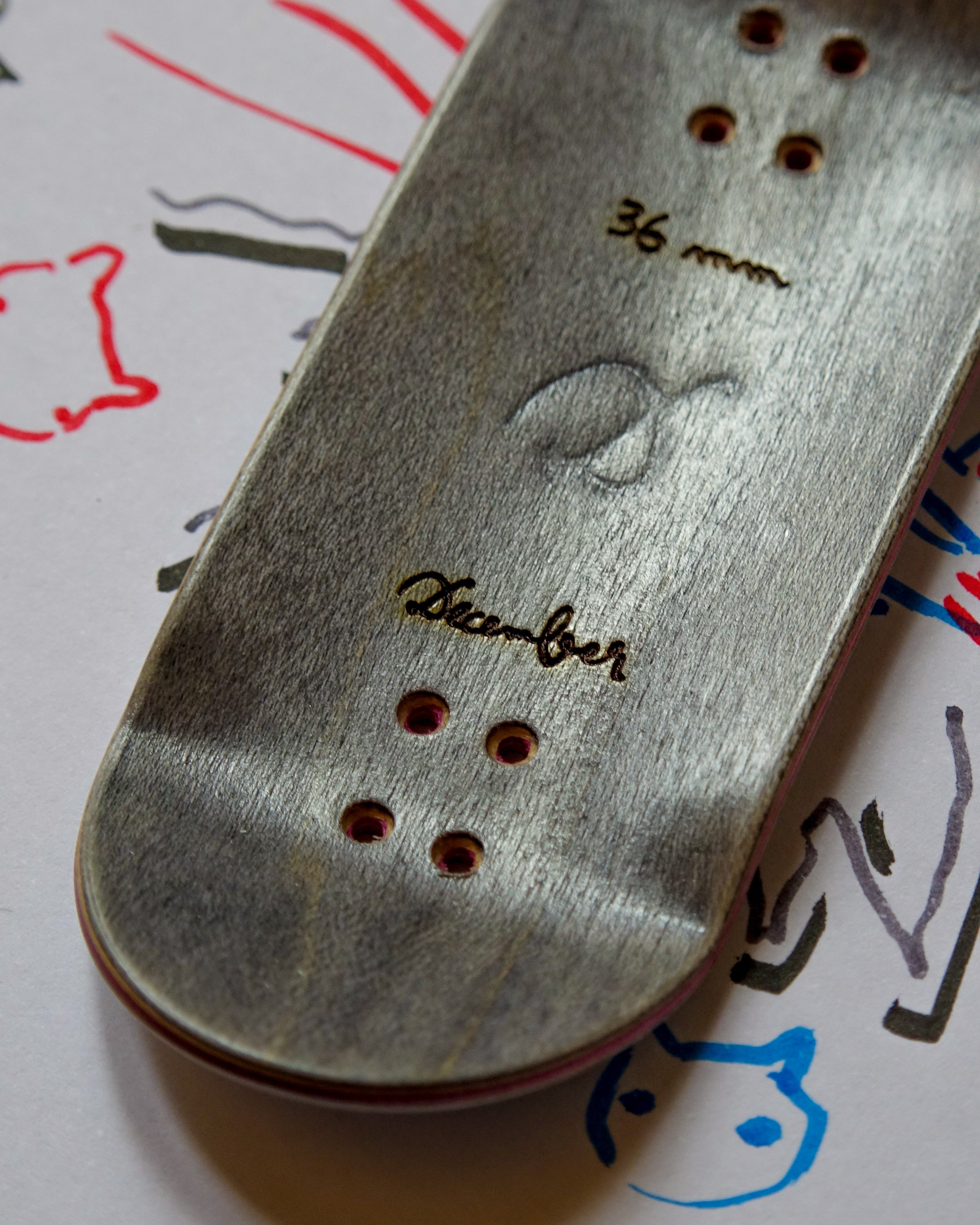 Close-up of a fingerboard deck with December branding on a surface with drawings.